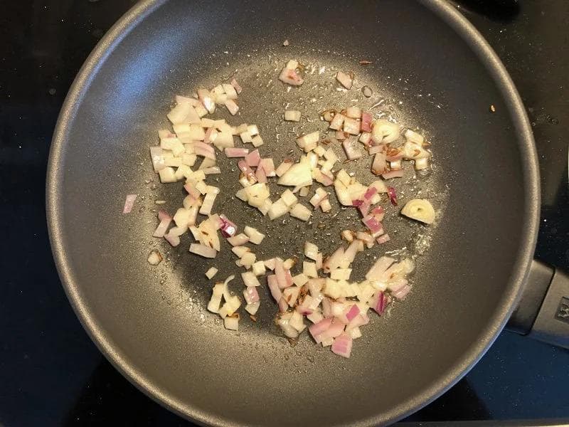 Diced onions and ham cooking in a dark pan with melted butter, partially softened.