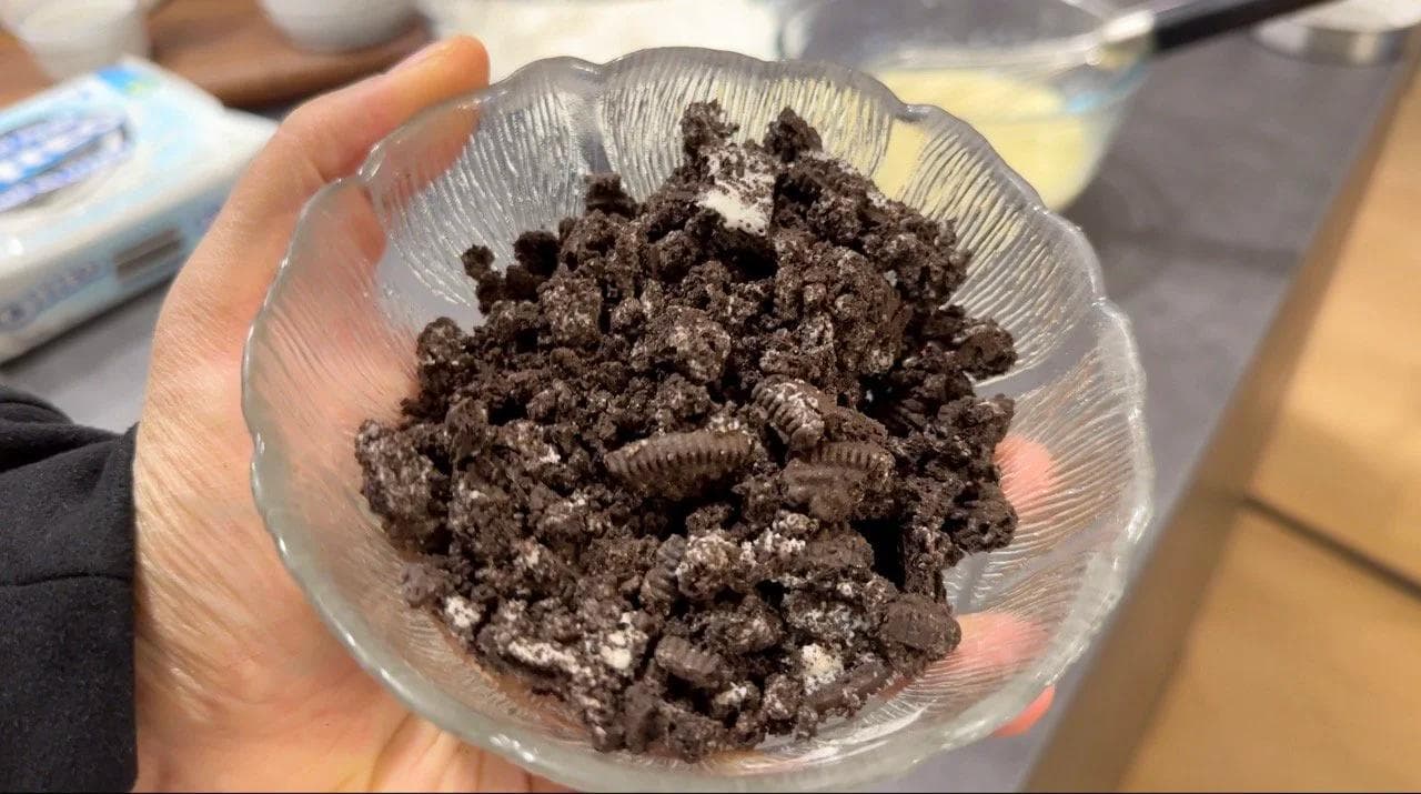 Crushed Oreo cookies mixed with flour in a glass bowl being held in someone's hand.