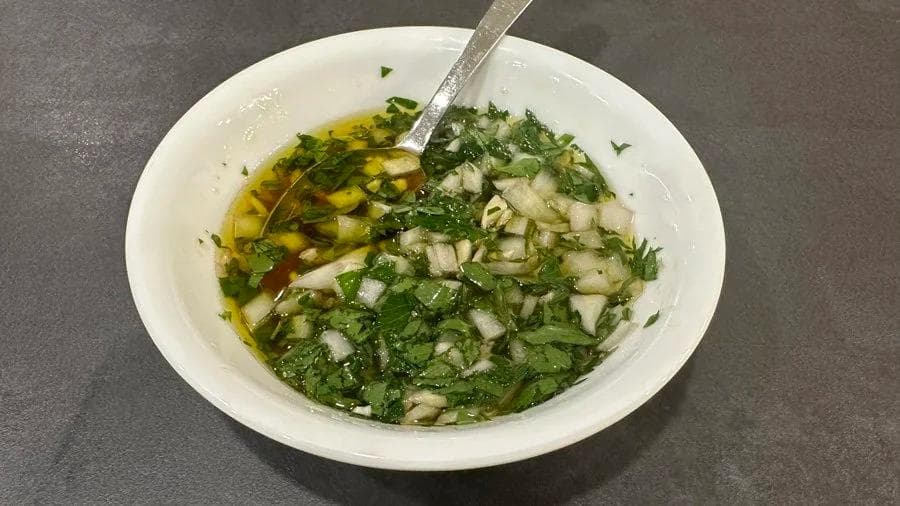 Chimichurri verde sauce in a white bowl with fresh parsley, garlic, and olive oil drizzle, with a spoon.