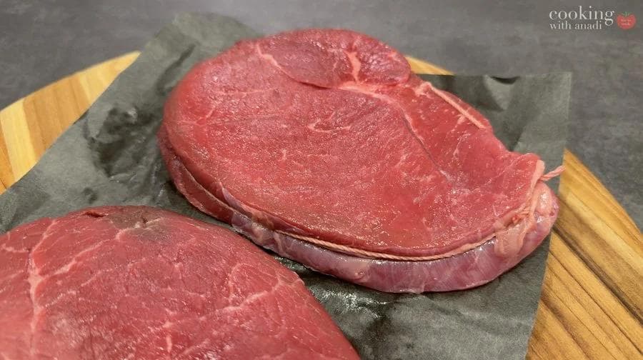 Two thick-cut sirloin steaks on parchment paper and wooden cutting board