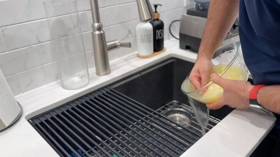 Hands squeezing shredded potatoes in a black kitchen sink strainer to remove excess water.
