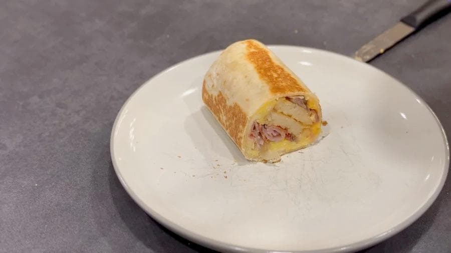 Toasted breakfast burrito with golden brown exterior on white plate, filled with eggs and meat.