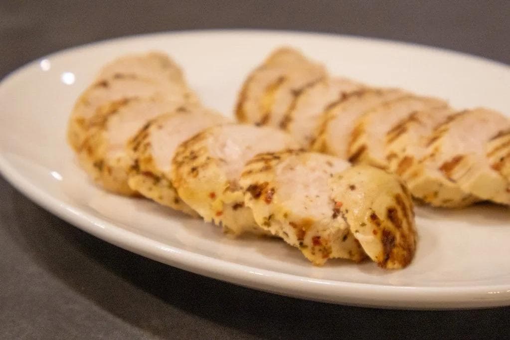 Sliced Italian herb grilled chicken breast on a white plate, showing grill marks and seasoning.