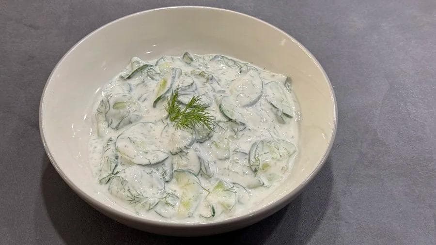 Creamy German cucumber salad with sliced cucumbers and fresh dill in a white bowl