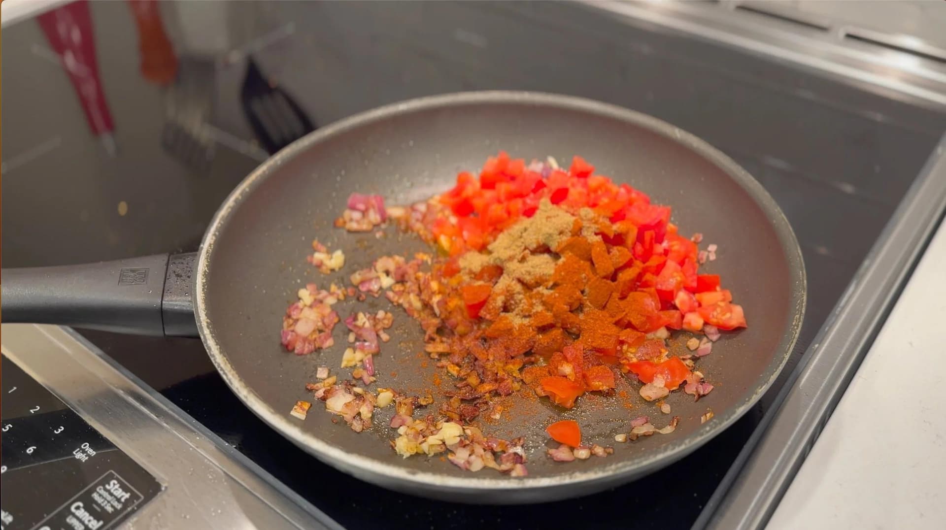Diced onions and red bell peppers cooking in a pan with spices during the sauté step of Mexican tomato rice.