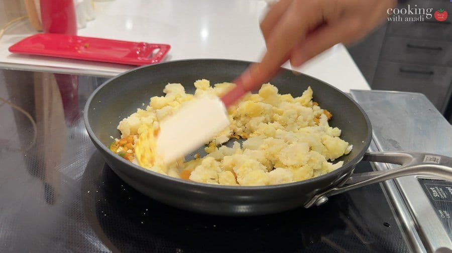 Cooked potatoes and onions mixed in a black pan with a piece of butter being added during preparation.