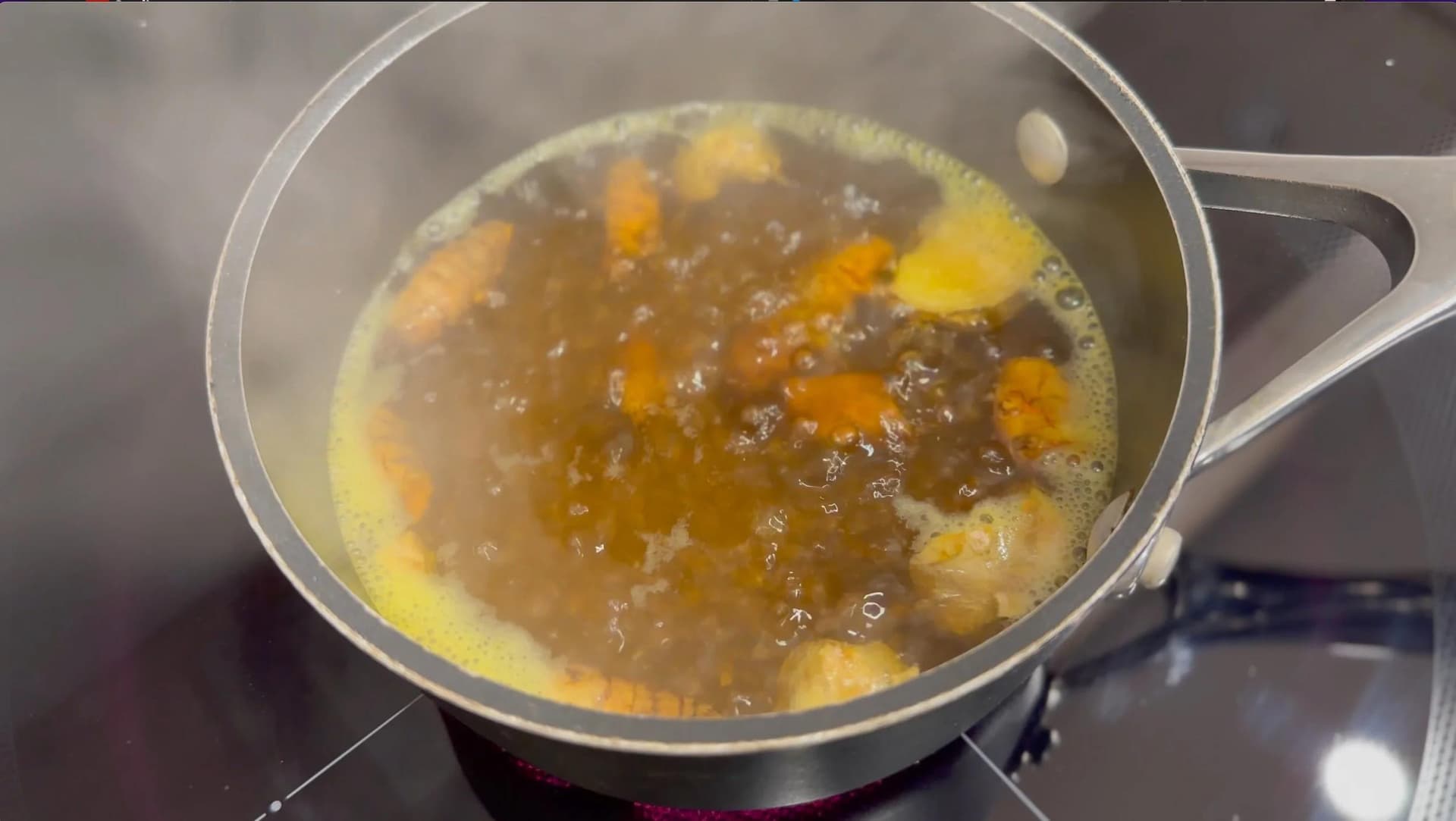 Turmeric chai latte simmering in saucepan with spices, ginger, and tea leaves boiling in water.