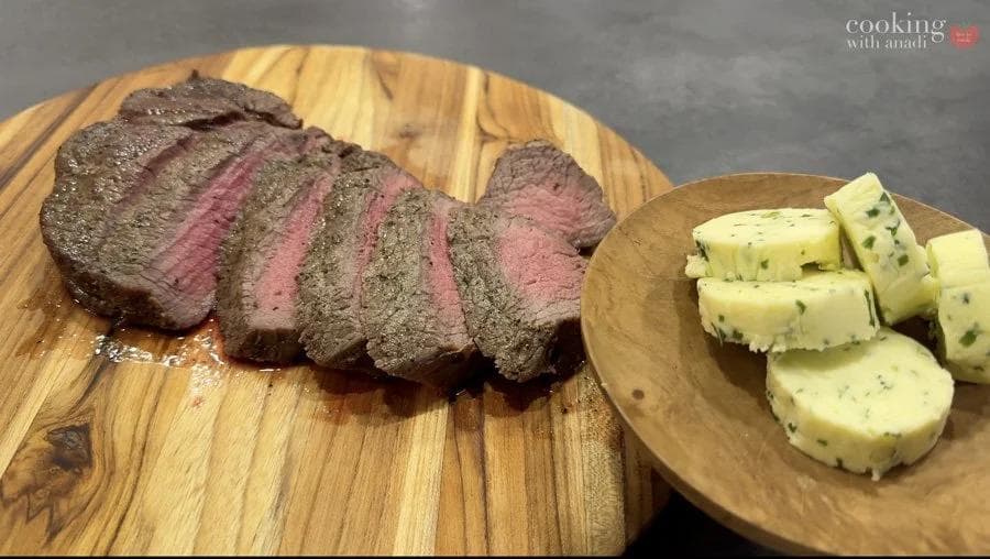 Sliced medium-rare air fryer sirloin steak topped with chive-garlic compound butter, served with butter pats on wooden boards.