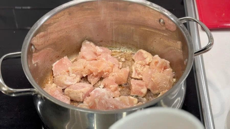 Browned chicken pieces in a pot with rendered bacon fat during the first steps of making chicken stew.