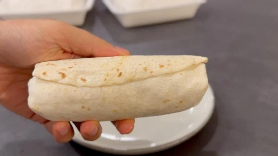 Hand holding a toasted breakfast burrito with golden brown exterior on a white plate.