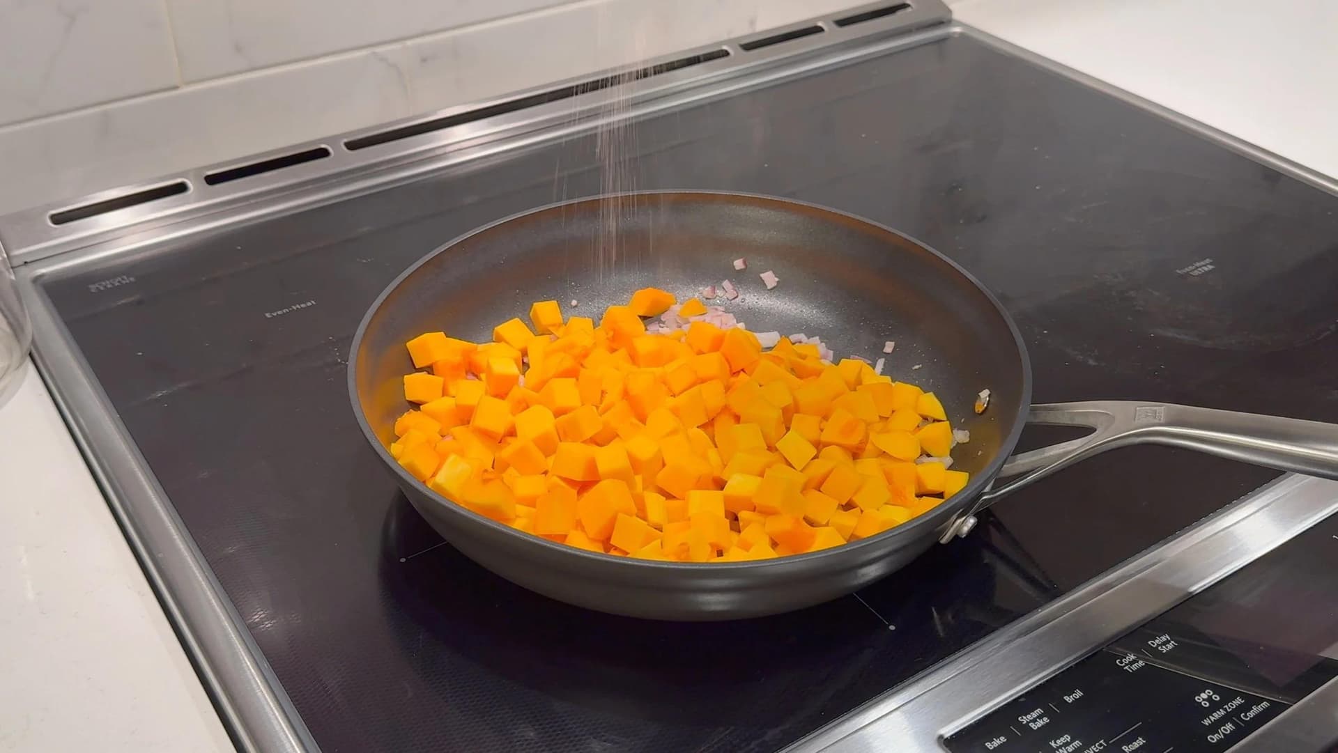 Diced butternut squash cooking in a skillet on an induction cooktop with lid partially visible.