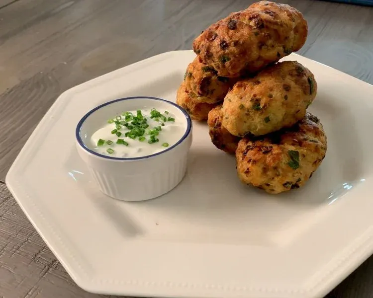 Three golden-brown air fryer chicken cutlets stacked on a white plate with a white dipping sauce topped with fresh chives.