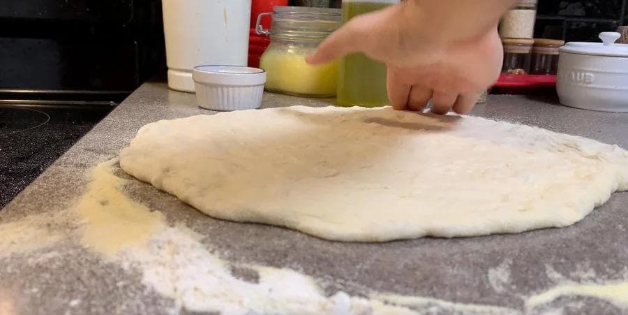 Hand pressing down and sealing the edges of pizza dough with a fork on a floured surface.