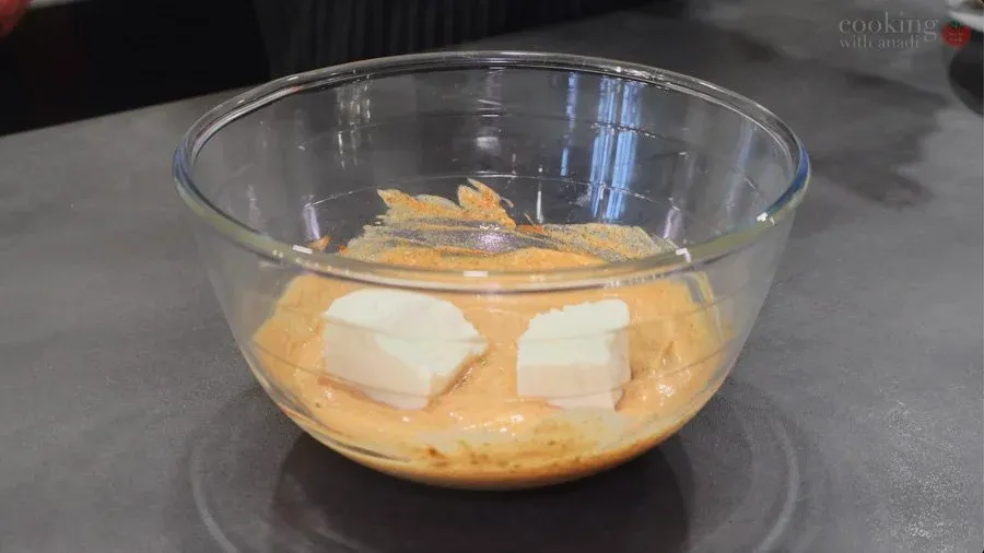 Paneer and vegetables coated in marinade with ghee in a glass bowl, ready to marinate.