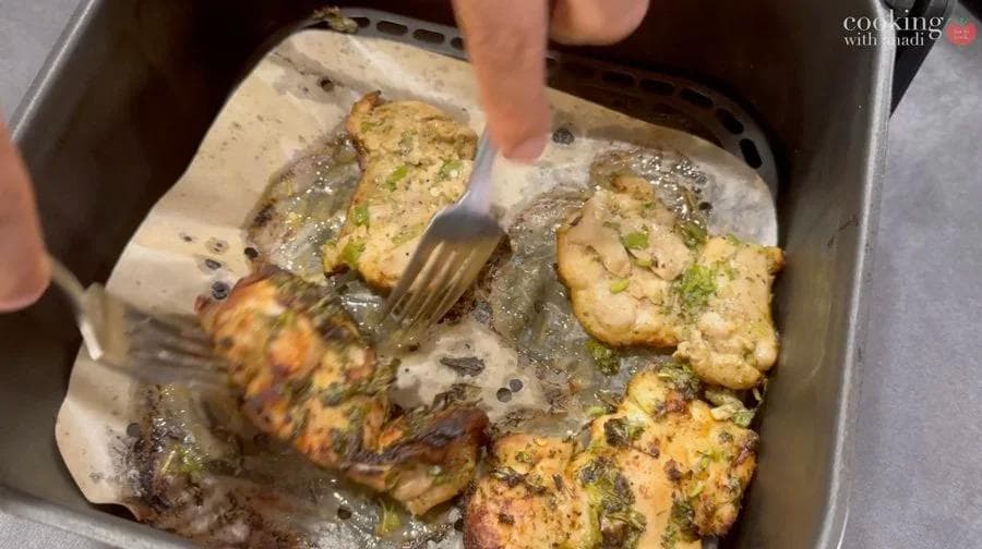 Cooked mojo chicken thighs with caramelized onions in an air fryer basket, being spooned with pan juices.