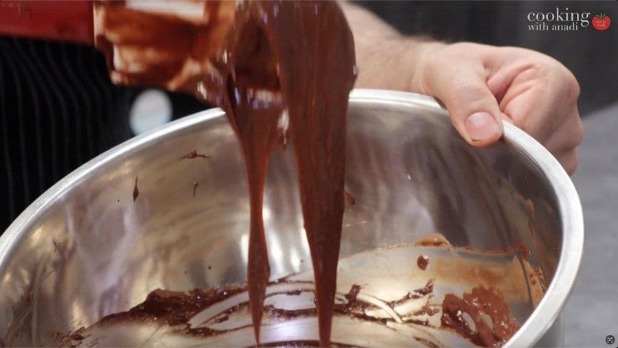 Folding melted chocolate into egg white mixture with a spatula in a metal bowl.