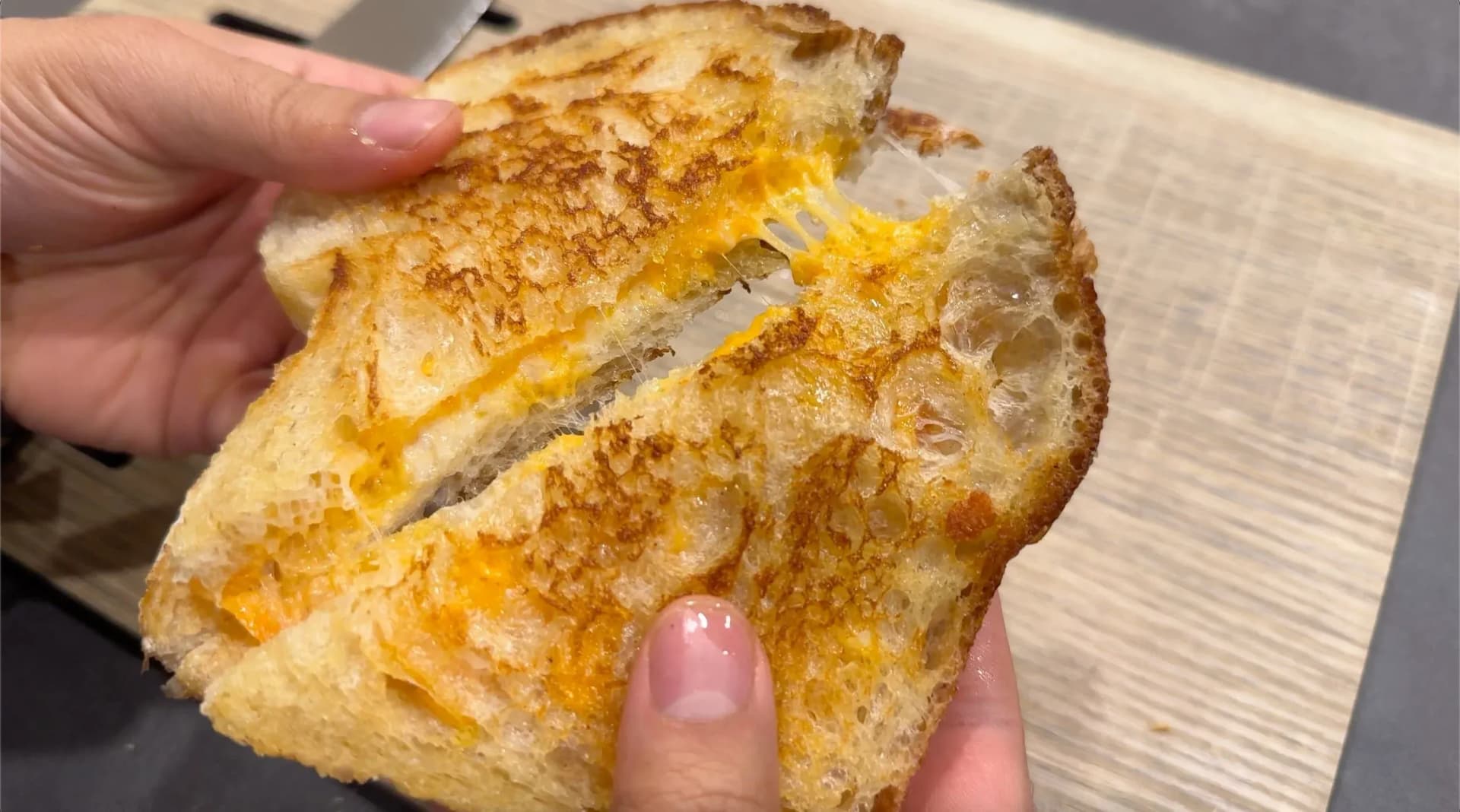 Golden-brown grilled cheese sandwich cut in half, showing melted yellow cheese between toasted bread slices.
