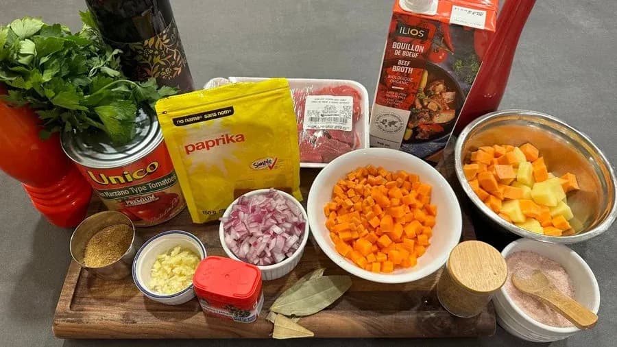 Ingredients laid out for Portuguese beef stew including paprika, diced onions, carrots, potatoes, and beef broth.