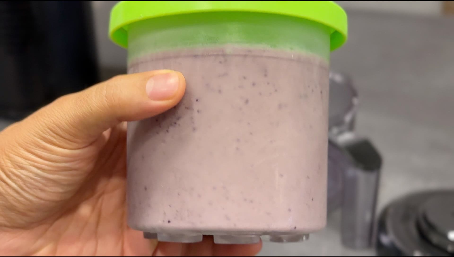 Hand holding a Ninja Creami jar with blueberry cheesecake protein ice cream after processing.