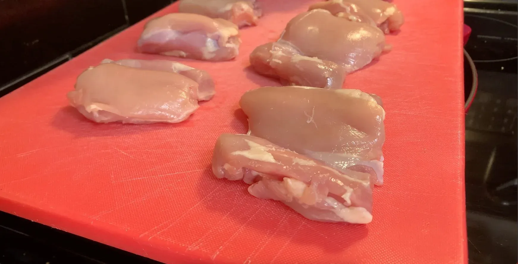 Raw chicken pieces patted dry and seasoned with salt and pepper on a pink cutting board.