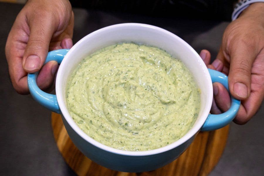 Creamy avocado lime crema in a white bowl with blue handles, held by hands.