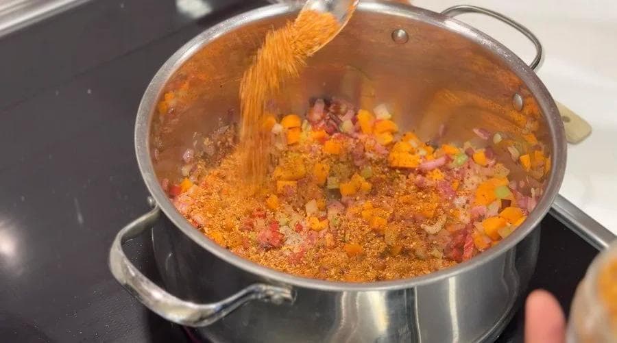 Spices being added to sautéed vegetables in a pot during harissa stew preparation