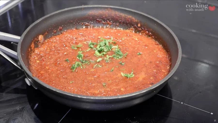 Simmered salsa roja in a dark skillet, garnished with fresh cilantro, on a stovetop.