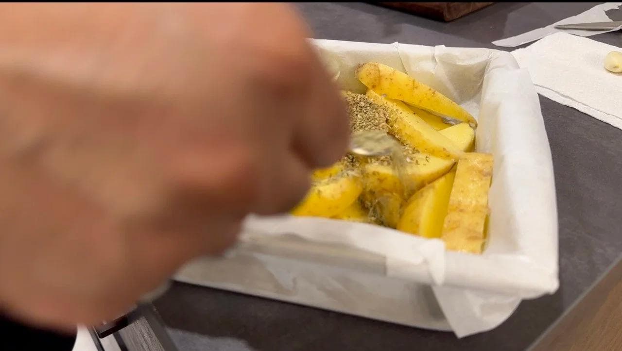 Seasoned potato wedges in a white container before baking, topped with herbs and lemon juice.