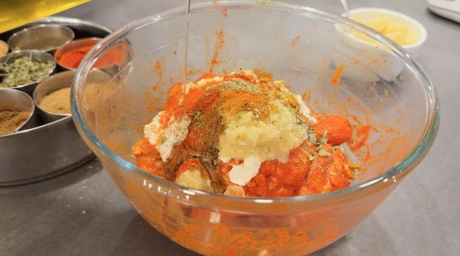 Second marinade mixture with yogurt, tomato paste, and spices in glass bowl ready to combine with chicken.