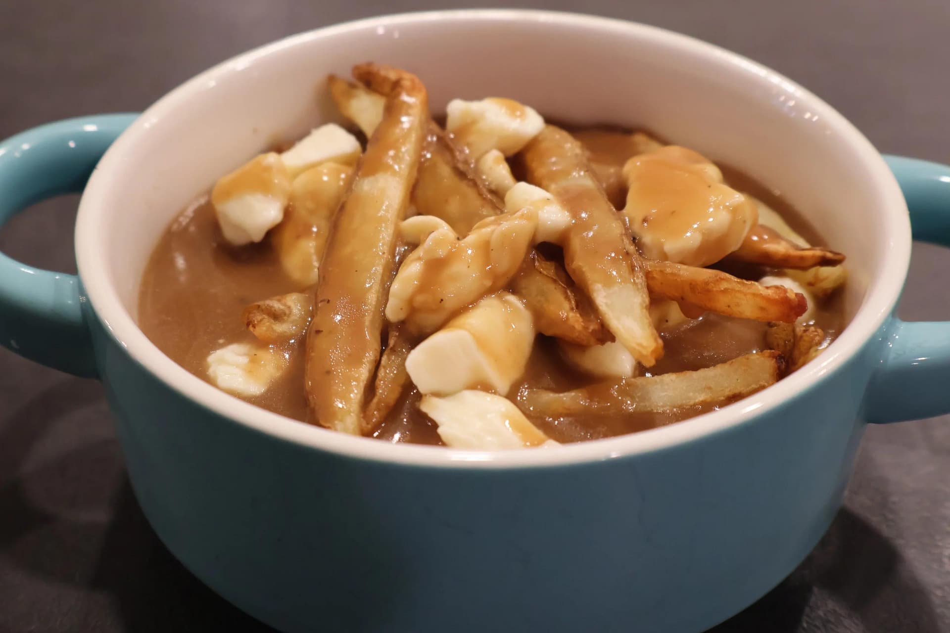 Poutine in a teal bowl with fries, cheese curds, and gravy, ready to serve.
