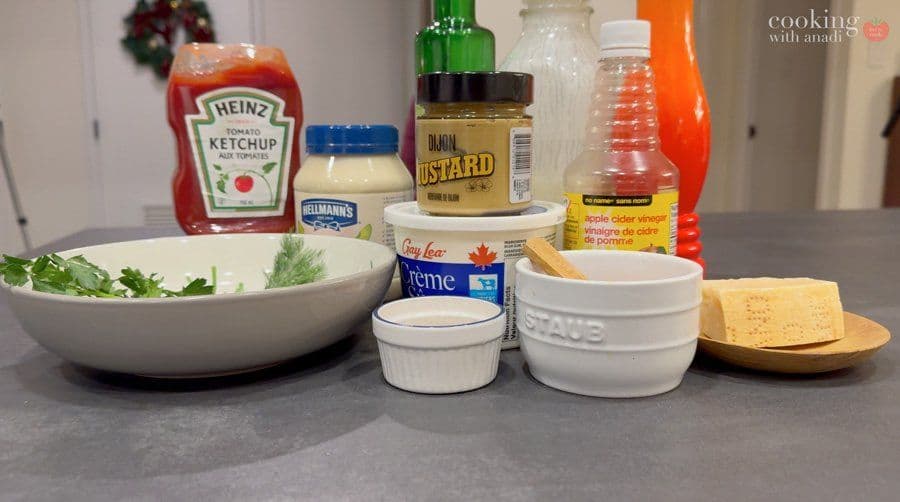 Ingredients for homemade ranch dip arranged on a counter, including mayonnaise, buttermilk, mustard, ketchup, and fresh herbs in a bowl.