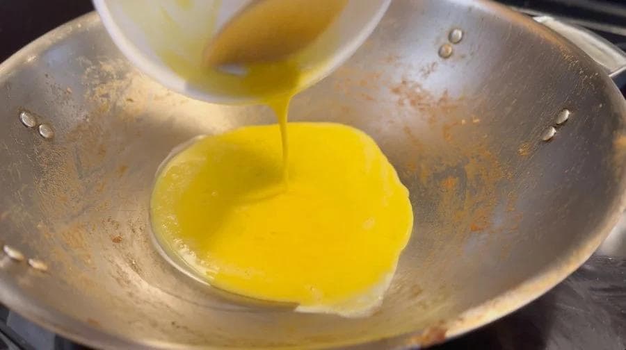 Scrambled eggs being poured into a hot wok for beef fried rice preparation.