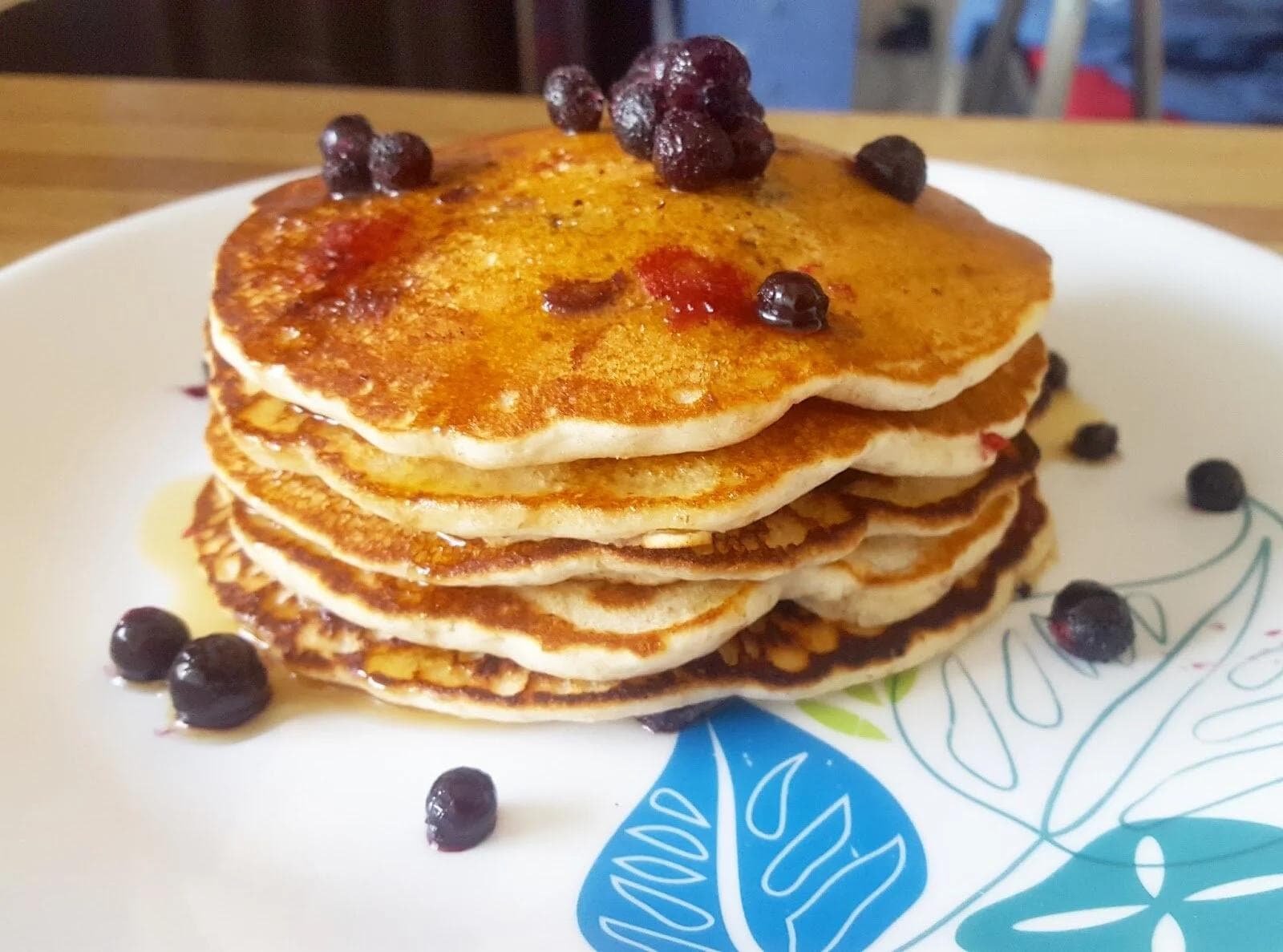 Stack of four fluffy pancakes topped with blueberries and raspberries on a white plate with decorative blue leaf pattern.