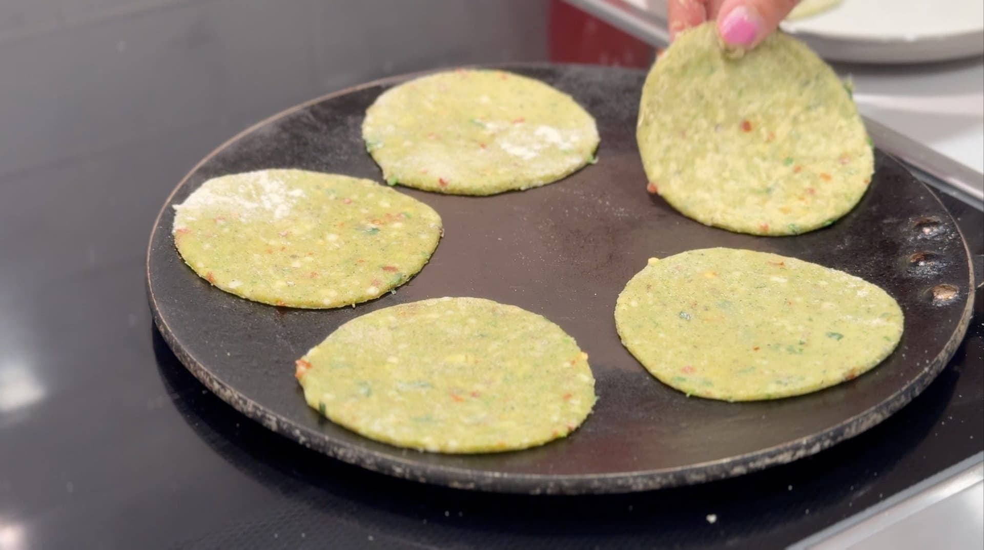 Five mini broccoli cheese parathas cooking on a dark griddle with golden brown spots.