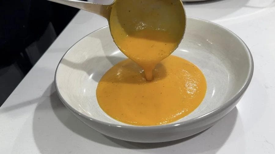 Creamy carrot and ginger soup being drizzled into a white bowl with a swirl of coconut milk on top.