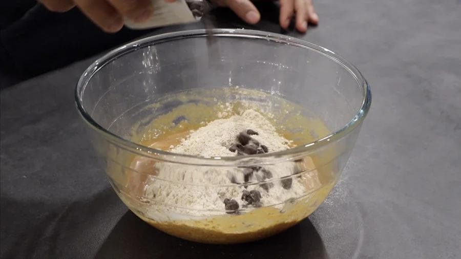 Wet and dry ingredients being combined in a glass bowl with chocolate chips folded in for pumpkin cookie dough.