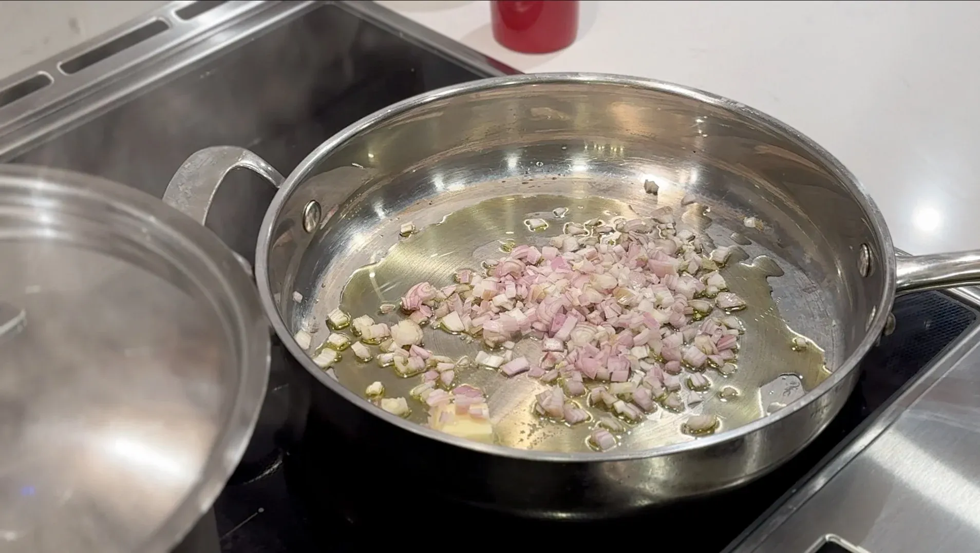 Diced shallots and pancetta cooking in olive oil and butter in a stainless steel pan on the stovetop.