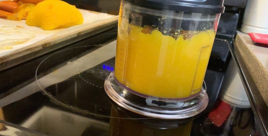 Food processor filled with smooth, thick orange pumpkin puree on a kitchen counter.