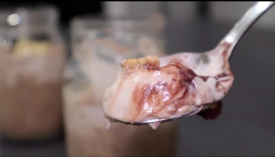 Spoonful of tiramisu overnight oats with cocoa powder topping and mascarpone mixture, held over glass jars.