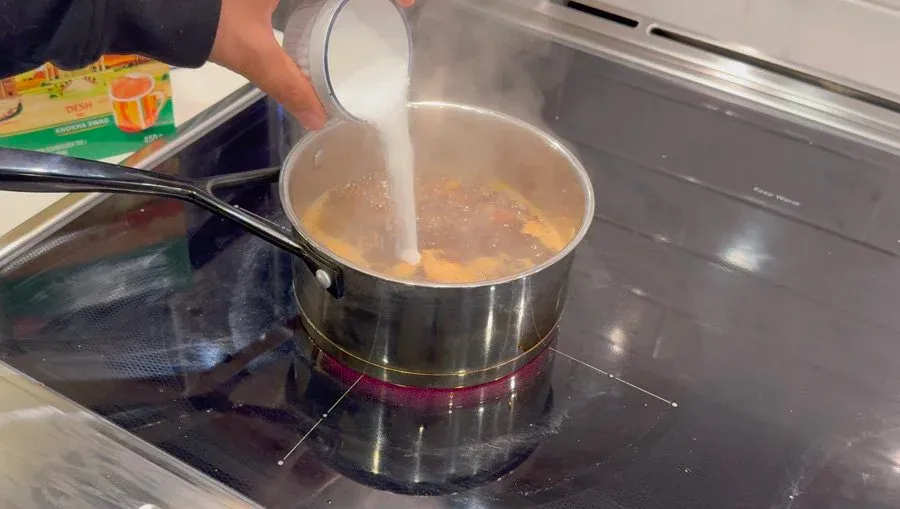Pouring milk into a saucepan of simmering chai tea on the stovetop.