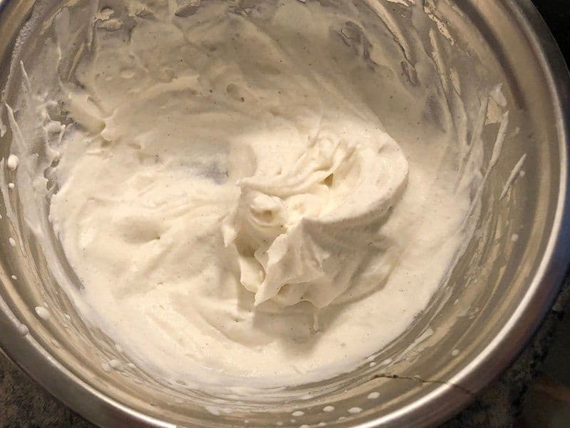 Over-whipped cream with stiff peaks in a metal bowl showing grainy, curdled texture