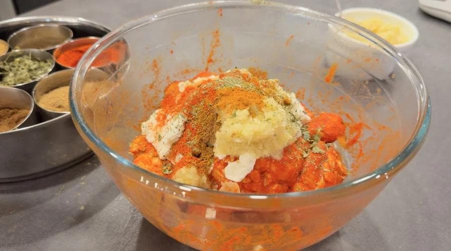 Clear bowl with tandoori chicken marinade ingredients mixed together, showing yogurt, spices, and tomato paste.