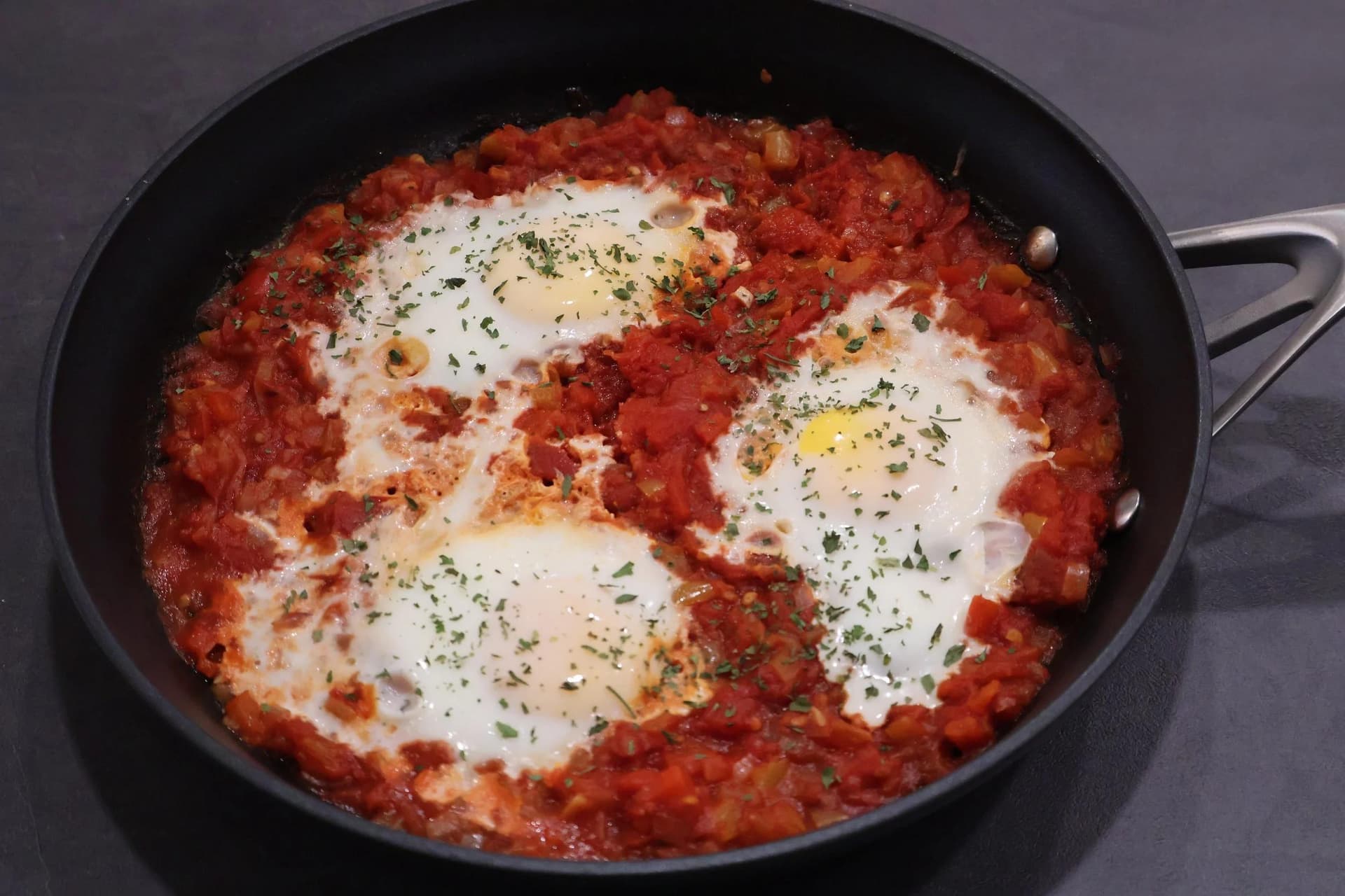 Shakshuka-style piperade with eggs poached in chunky tomato sauce, garnished with fresh herbs, in a black skillet.
