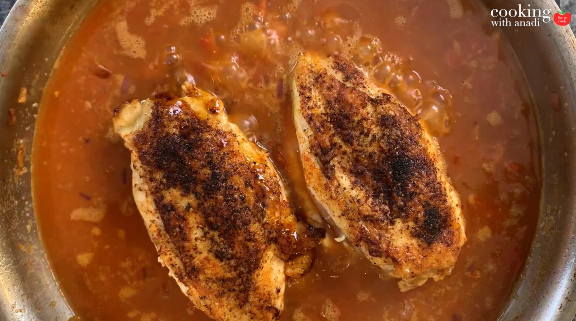 Two seasoned chicken breasts nestled in spiced rice and broth in a covered pot during baking.