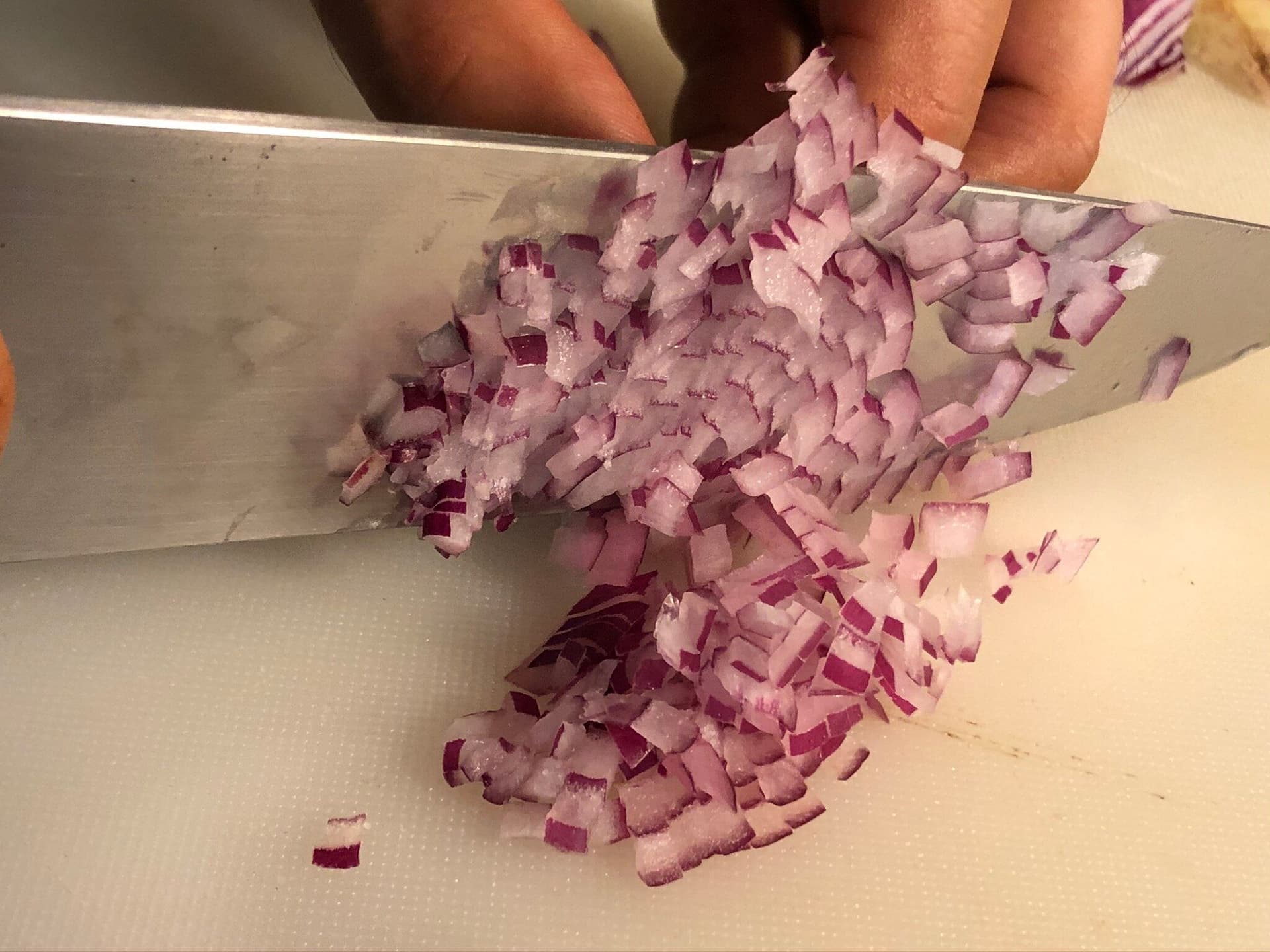 Chopped red onions on a cutting board with a knife, prepared for North Indian Poha recipe.