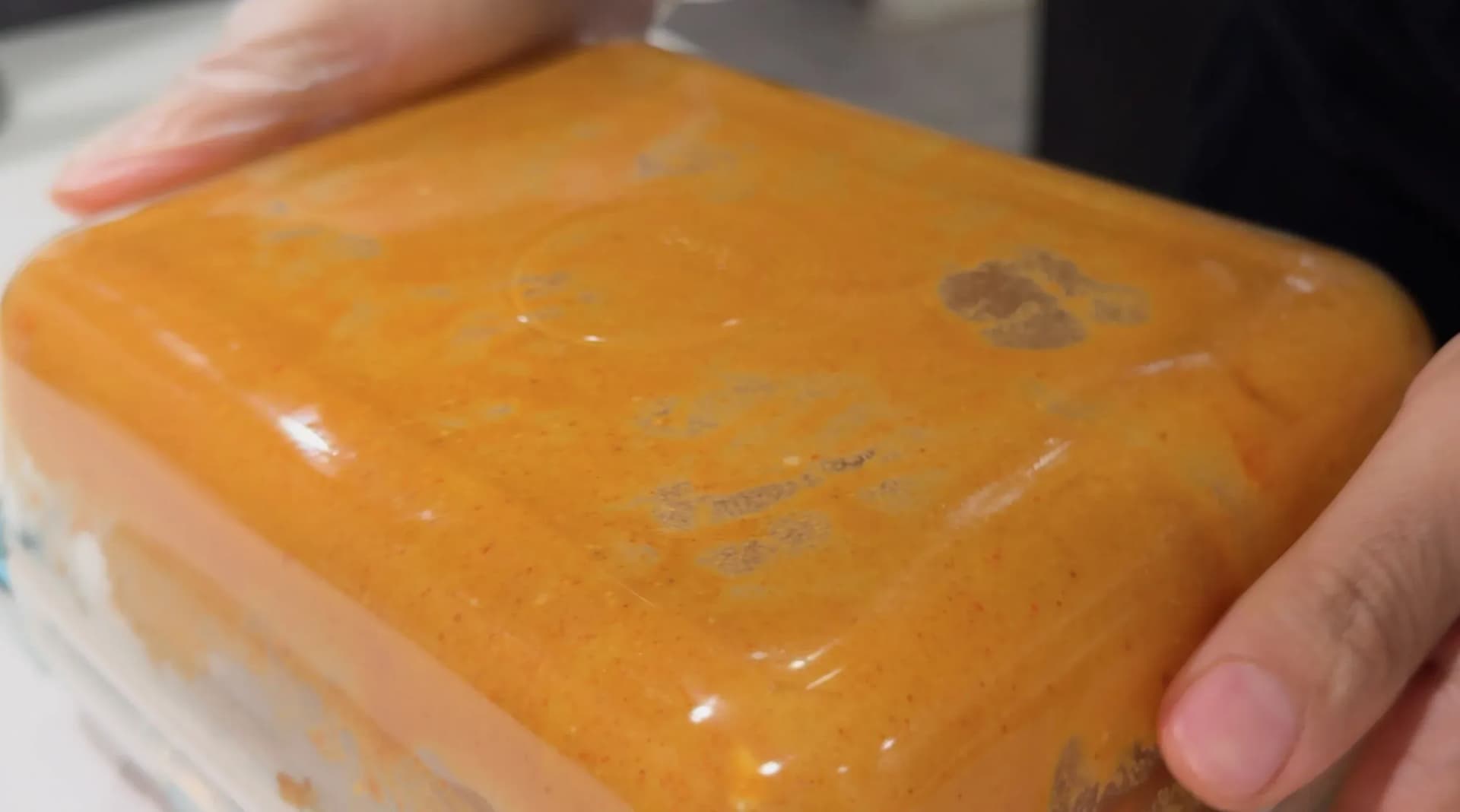 Paneer cubes coated in thick orange-red chilli batter, held in hands before air frying