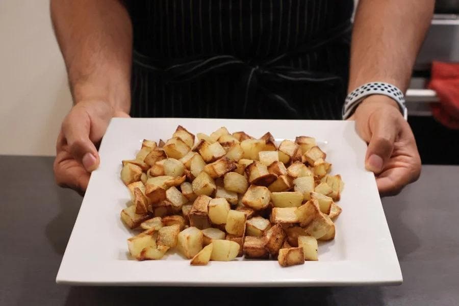 Crispy golden cubed roasted potatoes on a white plate held by hands.