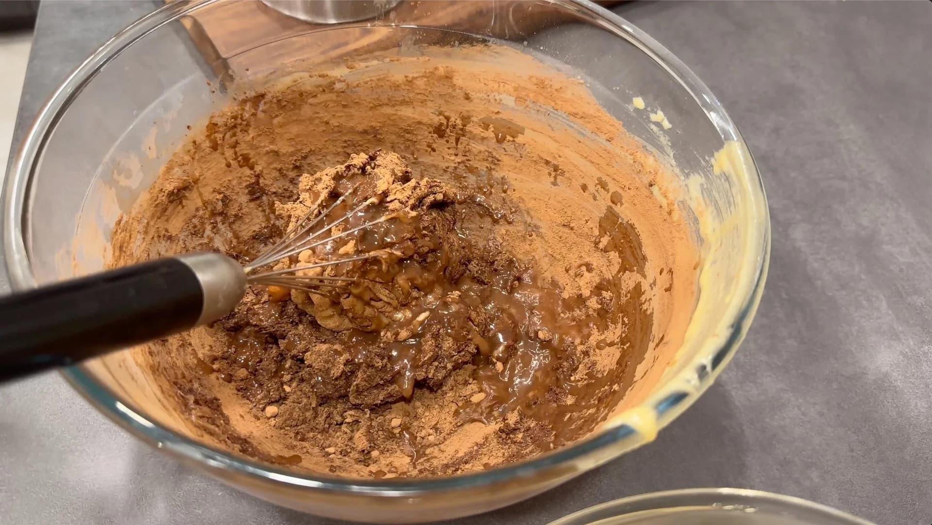 Chocolate batter being mixed in a glass bowl with a whisk, showing a thick, uniform cocoa-colored mixture.