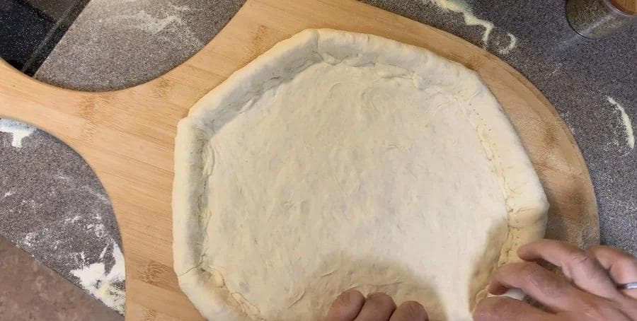 Hands pricking dough edges with a fork to seal the stuffed crust pizza on a wooden board.