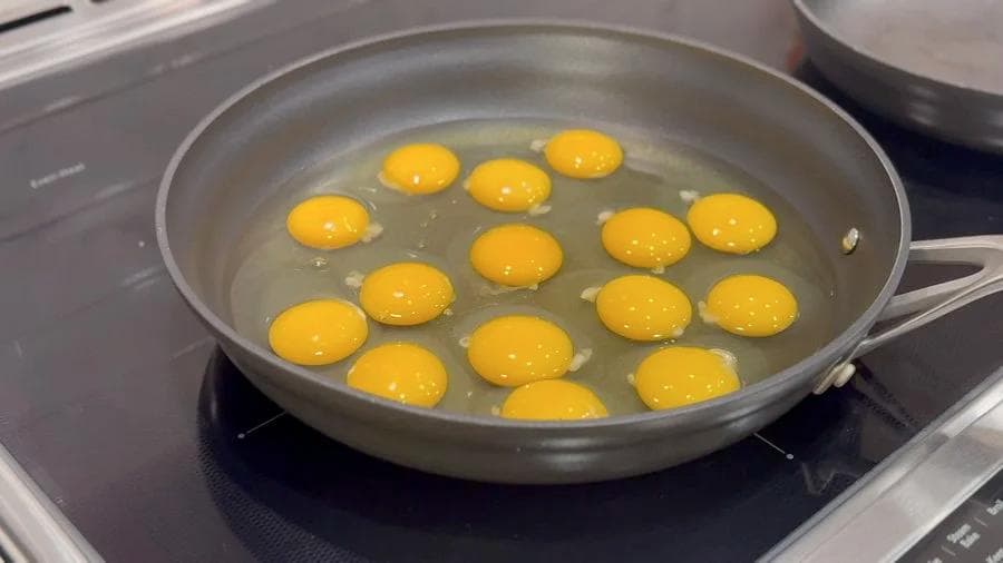 Multiple cracked eggs cooking in a skillet with melted butter on a stovetop.